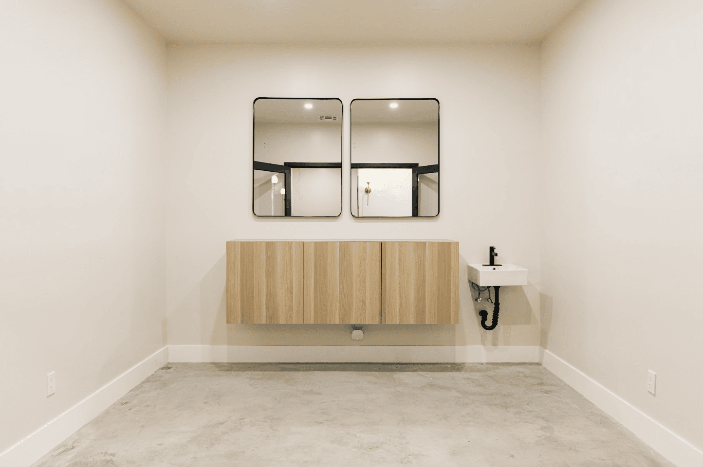 Clean, minimalist salon interior with mirrors, wooden cabinet, and small sink for clients.